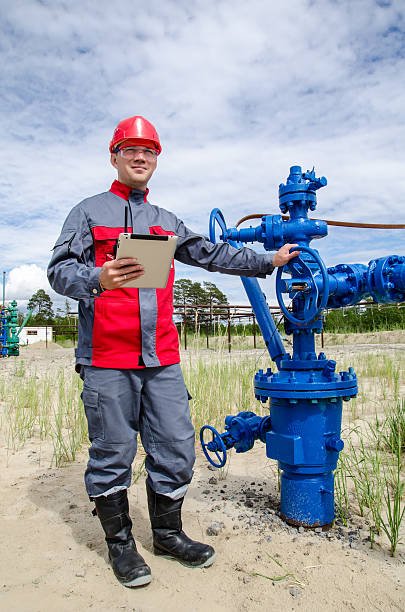 Worker near well head valve holding tablet computer  and radio and wearing red helmet in the oilfield. Oil and gas concept.